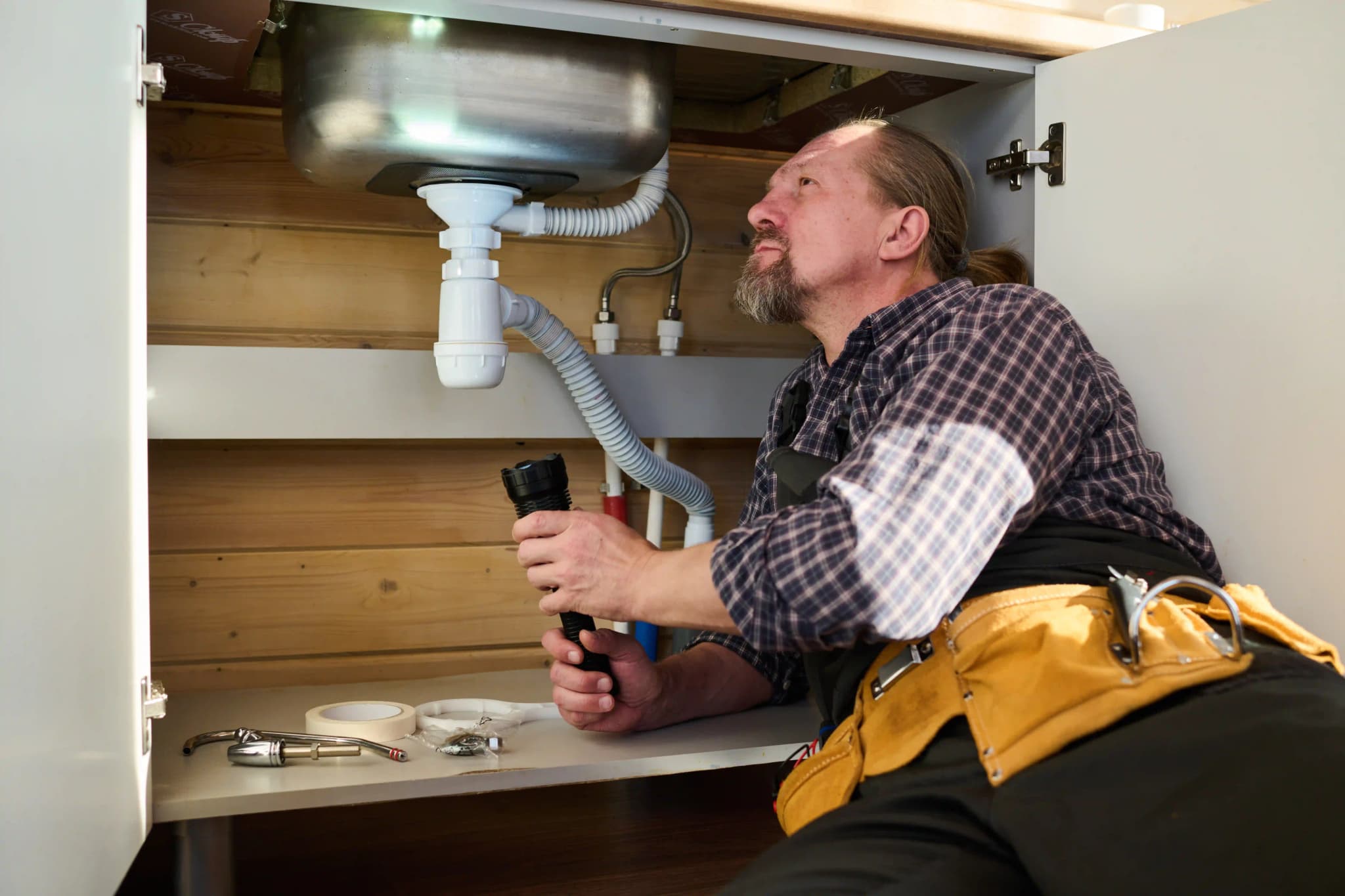 repairman-directing-flashlight-on-pipe-under-sink